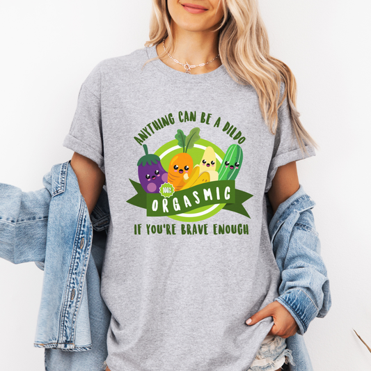 A woman wearing a grey graphic t-shirt with a colorful cartoon vegetable design and the text 'ANYTHING CAN BE A DILDO IF YOU'RE BRAVE ENOUGH'. She has a light blue denim jacket draped off her shoulders against a plain white background. purchase from Coffee and Moo NZ