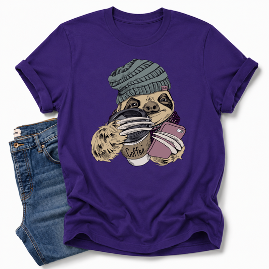 A purple short-sleeve crewneck t-shirt featuring a cartoon sloth wearing a green beanie and holding a coffee cup and a phone, styled flat-lay with a pair of blue denim shorts on a white background. Grab your tee from Coffee and Moo NZ.