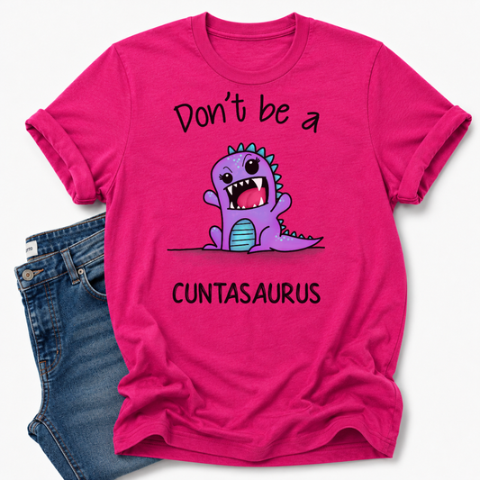 A bright pink graphic t-shirt featuring a cute purple cartoon dinosaur and the text 'Don't be a CUNTASaurus', styled flat-lay next to a pair of blue jeans on a white background. Grab your tee from Coffee and Moo NZ.