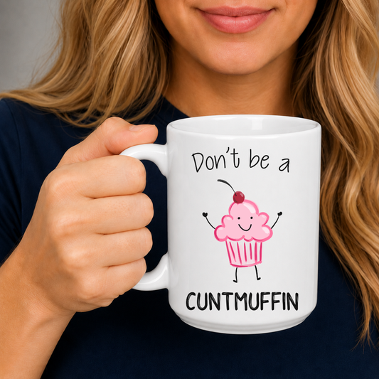 A female holding a white ceramic mug with a pink cupcake graphic and the text 'Don't be a CUNTMUFFIN' in black lettering. The person has blonde hair and is wearing a dark navy top against a neutral gray background. Grab yours from Coffee and Moo NZ.