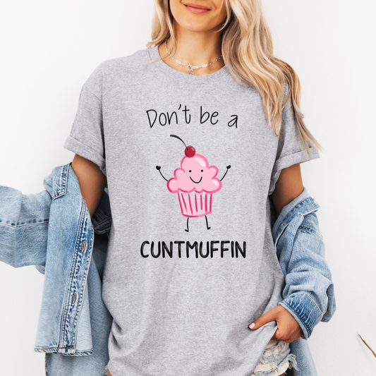 A woman wearing a heather gray graphic t-shirt with a cute pink cupcake character and the text 'Don't be a CUNTMUFFIN'. She has a light blue denim jacket draped off her shoulders against a plain white background. Purchase from Coffee and Moo NZ.