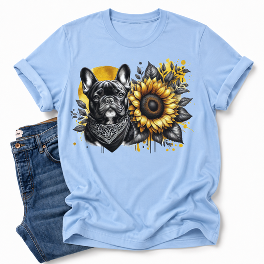 A light blue short-sleeve t-shirt with a graphic print of a French Bulldog wearing a bandana next to a large sunflower, styled flat-lay with a pair of blue jeans on a white background. Grab your tee from Coffee and Moo NZ.
