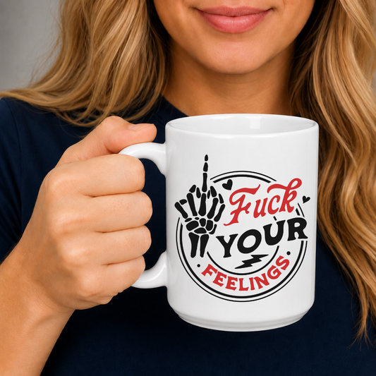 A person holding a white ceramic mug with a bold graphic that reads 'Fuck Your Feelings' in black and red lettering, featuring a hand gesture illustration. The person is wearing a dark navy blue shirt against a neutral gray background. Purchase from Coffee and Moo NZ.