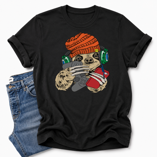 A black short-sleeve graphic T-shirt laid flat on a white background, styled with folded blue jeans at the lower left. The shirt features a colorful cartoon sloth wearing an orange knit beanie, green headphones, and holding a red phone and grey controller. Grab your tee from Coffee and Moo NZ.