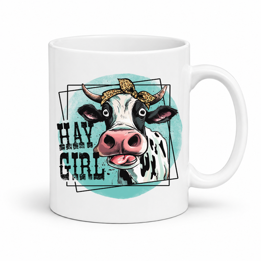 A white ceramic coffee mug featuring a graphic illustration of a cow with a leopard-print headband, set against a teal circle with the text 'HAY GIRL' in a distressed black font. from Coffee and Moo NZ.