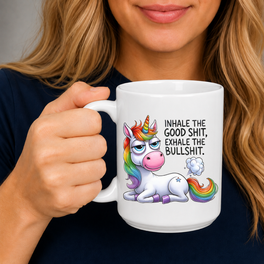A woman holding a white ceramic mug with a colorful cartoon unicorn and the text 'INHALE THE GOOD SHIT, EXHALE THE BULLSHIT.' Purchase from Coffee and Moo NZ.