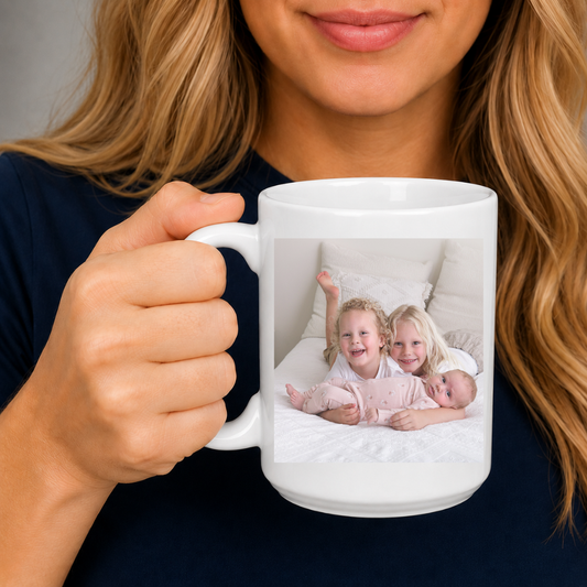 A mum holding a white ceramic mug with a custom printed family photo of two children and a baby on the front, set against a soft gray background. Grab your custom photo mug from Coffee and Moo