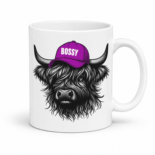 A white ceramic mug featuring a graphic illustration of a shaggy Highland cow wearing a purple cap with the word 'BOSSY' in white text, shown on a clean white background. Grab your bossy highland coo mug from Coffee and Moo NZ.