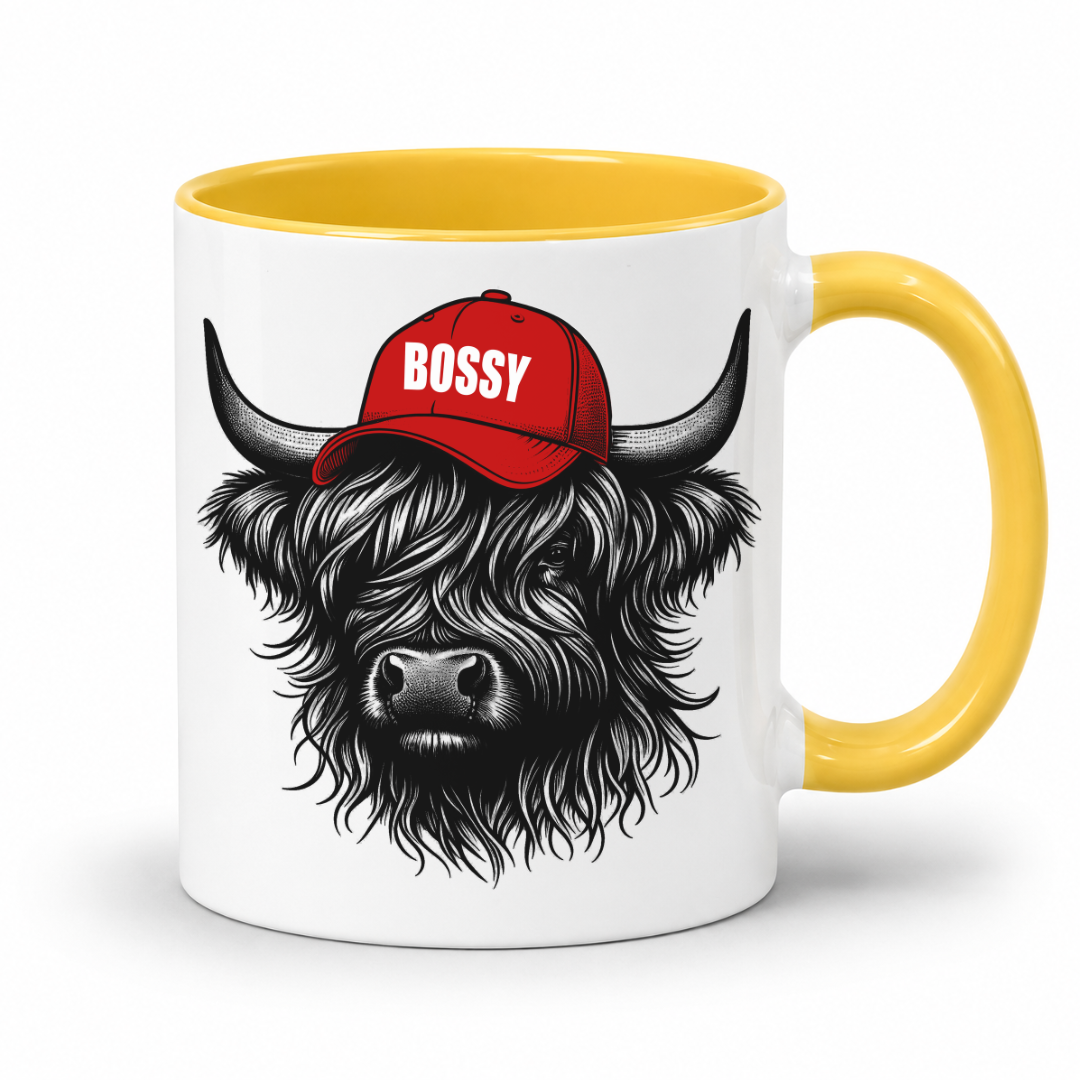 A white ceramic mug with a yellow interior and yellow handle, featuring a black-and-white illustration of a shaggy Highland cow wearing a red baseball cap with the word 'BOSSY' in white. Grab your Bossy highland coo mug from Coffee and Moo NZ.