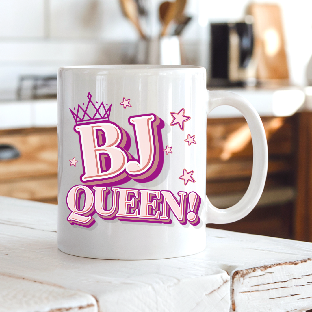 BJ Queen funny rude coffee mug on a country kitchen bench, featuring a crown, stars and bold pink BJ Queen lettering, by Coffee and Moo.
