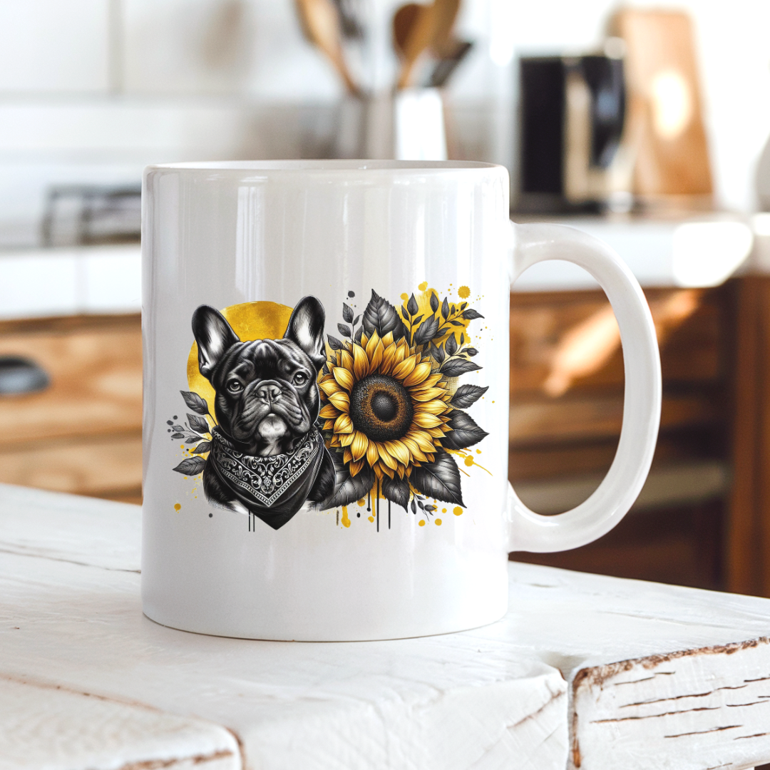 A white ceramic coffee mug with a graphic print of a French bulldog wearing a bandana next to a large sunflower, set on a rustic white wooden bench in a blurred kitchen background. Grab your frenchie mug from Coffee and Moo NZ