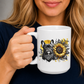 A woman holding a white ceramic mug with a graphic design of a black French Bulldog wearing a bandana next to a yellow and black sunflower. Grab your frenchie mug from Coffee and Moo NZ