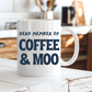 A white ceramic coffee mug with the text 'HERD MEMBER OF COFFEE & MOO' printed in dark navy blue, sitting on a rustic white wooden table in a warm, blurred kitchen setting. Grab your mug from Coffee and Moo NZ.