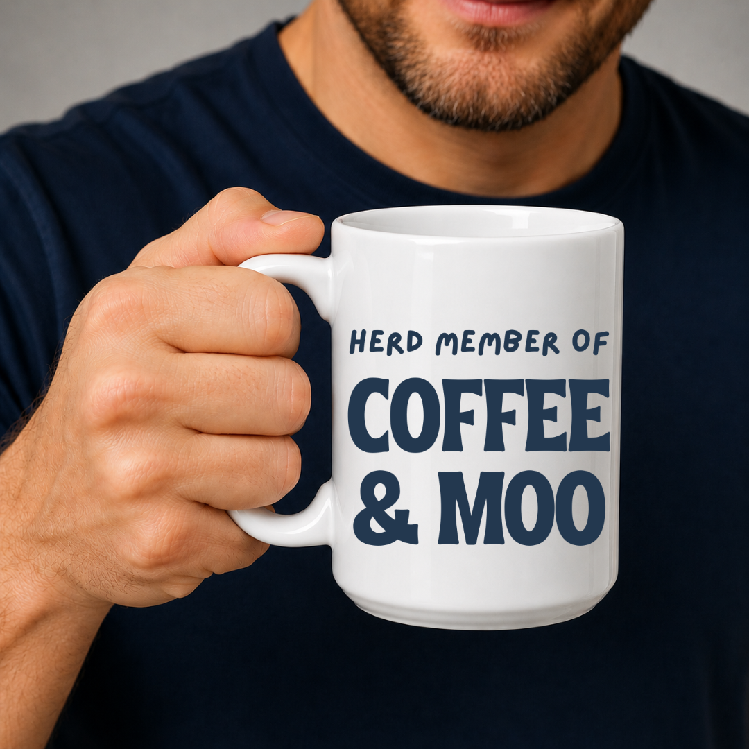 A man in a navy blue t-shirt holds a white ceramic mug with the text 'HERD MEMBER OF COFFEE & MOO' printed in navy blue lettering. Grab your mug from Coffee and Moo NZ.