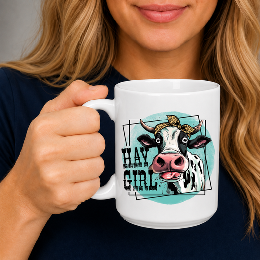 A woman holding a white ceramic mug with a graphic of a cow and the text 'HAY GIRL' on a dark navy shirt.  from Coffee and Moo NZ.