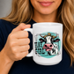 A woman holding a white ceramic mug with a graphic of a cow and the text 'HAY GIRL' on a dark navy shirt.  from Coffee and Moo NZ.