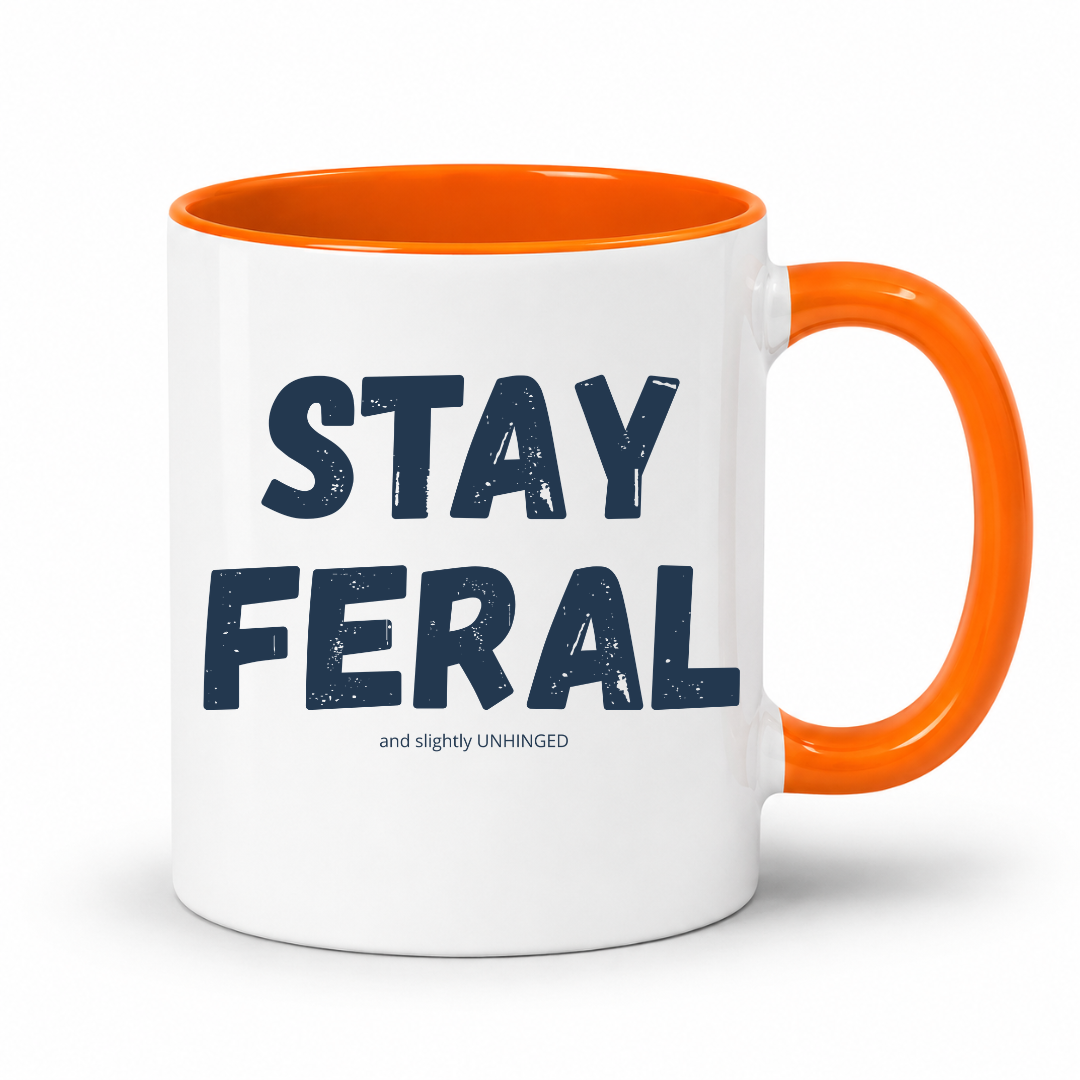 A white ceramic coffee mug with a bright orange handle and interior, featuring the text 'STAY FERAL and slightly UNHINGED' printed in dark navy blue on the front, set against a plain white background. Grab your feral mug from Coffee and Moo NZ.