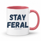 A white ceramic coffee mug with a pink interior and handle, featuring the text 'STAY FERAL' in dark navy blue letters and 'and slightly UNHINGED' in smaller text below, on a white background. Grab your feral mug from Coffee and Moo NZ.