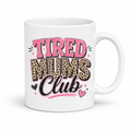 A white ceramic mug featuring a graphic design that reads 'TIRED MUMS Club' in pink, leopard print, and black lettering with small heart and star accents, set against a plain white background. Grab your mug from Coffee and Moo NZ.