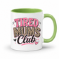 A white ceramic mug with a light green handle and interior, featuring the text 'TIRED MUMS Club' in pink, leopard print, and black lettering on the front. Grab your mug from Coffee and Moo NZ.