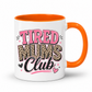 A white ceramic mug with a bright orange handle and interior, featuring the text 'TIRED MUMS Club' in pink, leopard print, and black lettering on the front. Grab your mug from Coffee and Moo NZ.