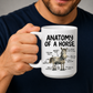 A white ceramic mug with a humorous 'Anatomy of a Horse' illustration and text, held by a man wearing a navy blue t-shirt against a neutral gray background. From Coffee and Moo NZ.
