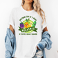 A woman wearing a white graphic t-shirt with a colorful cartoon vegetable design and the text 'ANYTHING CAN BE A DILDO' 'IF YOU'RE BRAVE ENOUGH', She has a light blue denim jacket draped off her shoulders. purchase from Coffee and Moo NZ