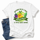 A white graphic t-shirt featuring cartoon vegetables and the text 'ANYTHING CAN BE A DILDO, IF YOU'RE BRAVE ENOUGH', styled flat-lay with blue jeans on a white background. Gra your tee from Coffee and Moo NZ.