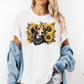 A woman wearing a white graphic t-shirt with a sunflower and beagle print, styled with a light blue denim jacket draped off her shoulders. Grab your tee from Coffee and Moo.