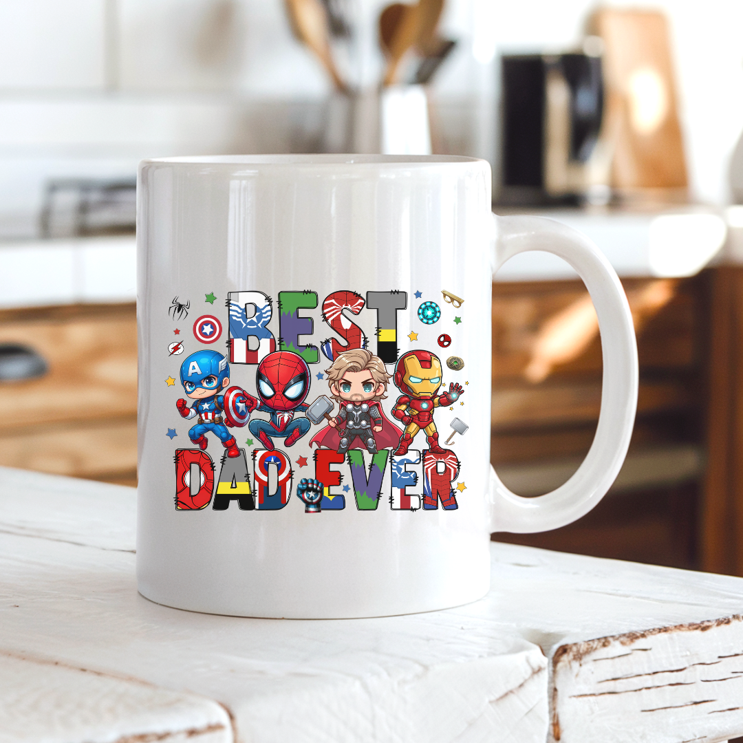 A white ceramic coffee mug with a colorful 'BEST DAD EVER' graphic featuring chibi Marvel superheroes, sitting on a rustic white wooden table in a blurred kitchen setting. Grab yours from Coffee and Moo