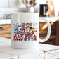 A white ceramic coffee mug with a colorful 'BEST DAD EVER' graphic featuring chibi Marvel superheroes, sitting on a rustic white wooden table in a blurred kitchen setting. Grab yours from Coffee and Moo
