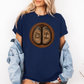 A woman wearing a navy graphic t-shirt with a circular design of two cow hooves reading 'Stay Feral' and 'Coffee & Moo'. She has a light blue denim jacket off her shoulders and is wearing denim shorts against a plain white background. Grab your official Coffee & Moo brand tee from Coffee and Moo NZ.