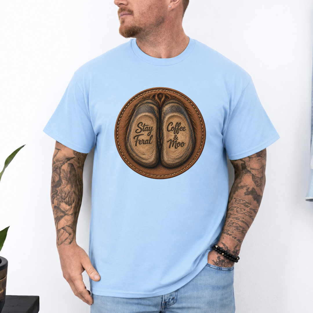 A man wearing a baby-blue short-sleeve graphic t-shirt with a circular print of two brown cow hooves reading 'Stay Feral' and 'Coffee Moo'.  Grab your official Coffee & Moo brand tee from Coffee and Moo NZ.