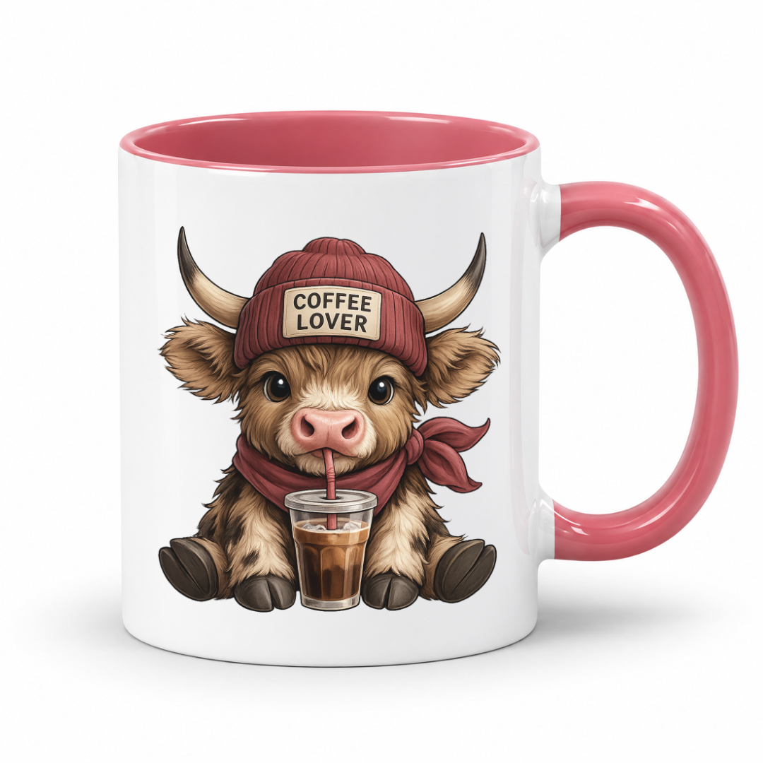 A white ceramic coffee mug with a pink interior, handle, and rim, featuring a cartoon illustration of a horned cow wearing a red beanie that says 'COFFEE LOVER' and holding a drink. from Coffee and Moo.