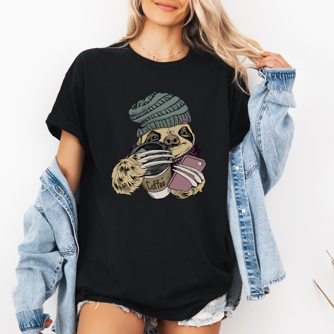 A woman wearing a black oversized graphic t-shirt with a sloth holding a coffee cup and phone, styled with an open light blue denim jacket. Grab your tee from Coffee and Moo NZ.