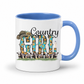 A white ceramic coffee mug with a blue interior and handle, featuring a 'Country Girl' graphic with a cowboy hat, sunflowers, and cows on a white background.  From Coffee and Moo NZ