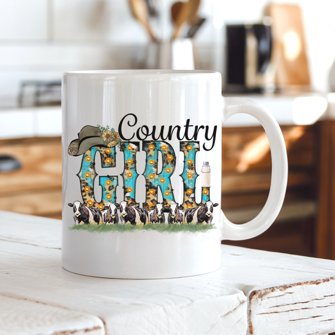 A white ceramic coffee mug with a 'Country Girl' graphic design, sitting on a rustic white wooden table with a blurred kitchen background.  From Coffee and Moo NZ