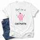 A white short-sleeve graphic T-shirt laid flat with blue jeans partially visible underneath on the left. The shirt has a printed cupcake illustration in pink and black text reading “Don’t be a CUNTMUFFIN. grab your tee from Coffee and Moo NZ.