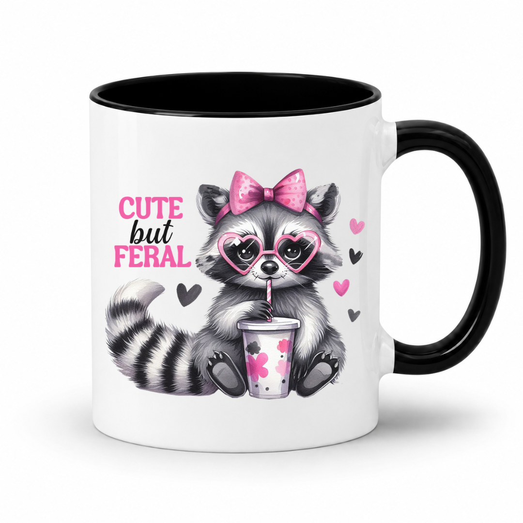A white ceramic mug with a black interior and black handle, featuring a cute cartoon raccoon wearing heart-shaped glasses and a pink bow, holding a drink, with the text 'CUTE but FERAL' on the front. from Coffee and Moo.