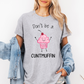 A woman wearing a heather gray graphic t-shirt with a cute pink cupcake character and the text 'Don't be a CUNTMUFFIN'. She has a light blue denim jacket draped off her shoulders against a plain white background. Purchase from Coffee and Moo NZ.