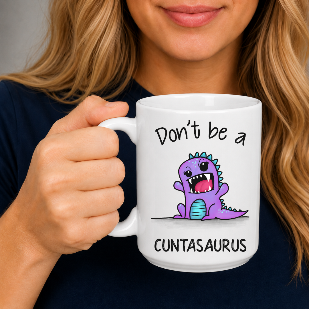 A person holding a white ceramic mug with a purple cartoon dinosaur and the text 'Don't be a CUNTASaurus'. Grab yours from Coffee and Moo NZ.