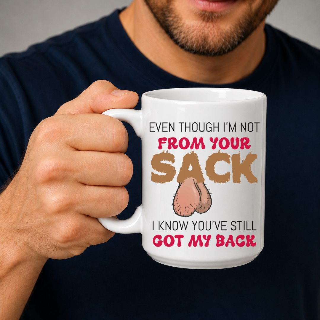 A man in a navy blue t-shirt holds up a white ceramic mug with a humorous graphic. The mug features the text 'EVEN THOUGH I'M NOT FROM YOUR SACK I KNOW YOU'VE STILL GOT MY BACK' in brown and red lettering, with a graphic of hairy balls in the center. Grab yours from Coffee and Moo NZ.