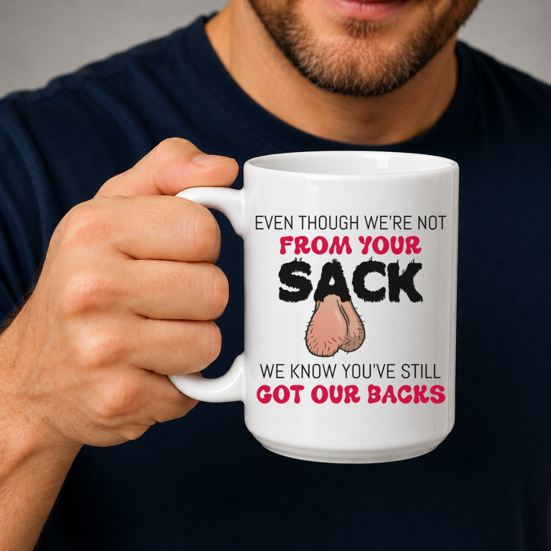 A man in a navy blue shirt holds a white ceramic mug with a humorous printed message The mug features the text 'EVEN THOUGH WE'RE NOT FROM YOUR SACK WE KNOW YOU'VE STILL GOT OUR BACKS' in black and red lettering, accompanied by a cartoon drawing of a hairy balls. Grab your mug from Coffee and Moo NZ.