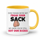 A white ceramic coffee mug with a yellow interior and handle, has a humorous graphic. The mug features the text 'EVEN THOUGH WE'RE NOT FROM YOUR SACK WE KNOW YOU'VE STILL GOT OUR BACKS' in black and red lettering, accompanied by a cartoon drawing of a hairy balls. Grab your mug from Coffee and Moo NZ.