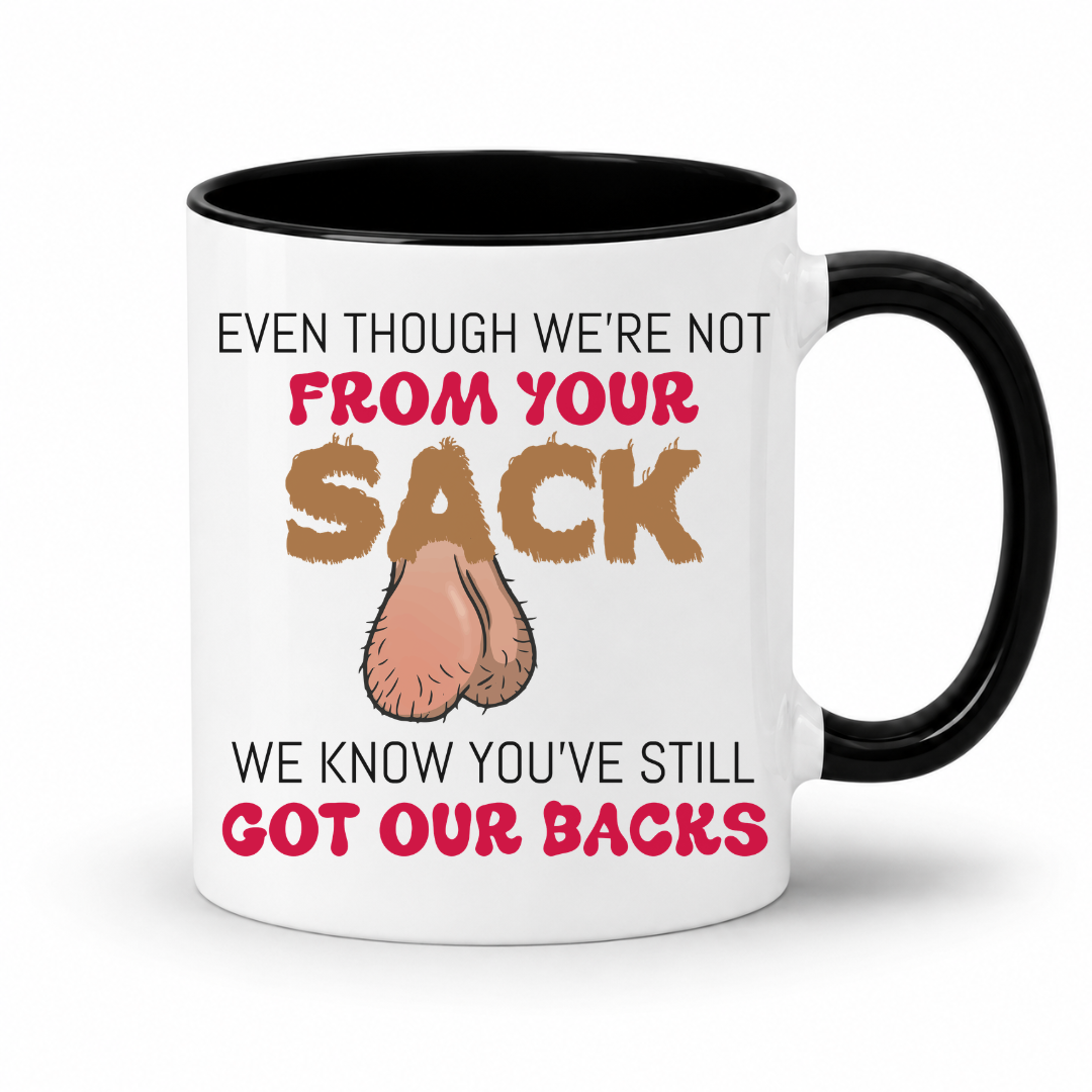 A white ceramic coffee mug with a black interior and handle, has a humorous graphic. The mug features the text 'EVEN THOUGH WE'RE NOT FROM YOUR SACK WE KNOW YOU'VE STILL GOT OUR BACKS' in brown and red lettering, accompanied by a cartoon drawing of a hairy balls. Grab your mug from Coffee and Moo NZ.
