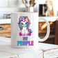 A white ceramic coffee mug with a cartoon unicorn graphic and the text 'EW PEOPLE' printed on it, sitting on a white wooden table in a blurred kitchen setting. from Coffee and Moo.