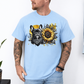 A man wearing a light blue graphic t-shirt featuring a French Bulldog and a sunflower design, paired with light blue jeans against a white wall. Grab your tee from Coffee and Moo NZ.