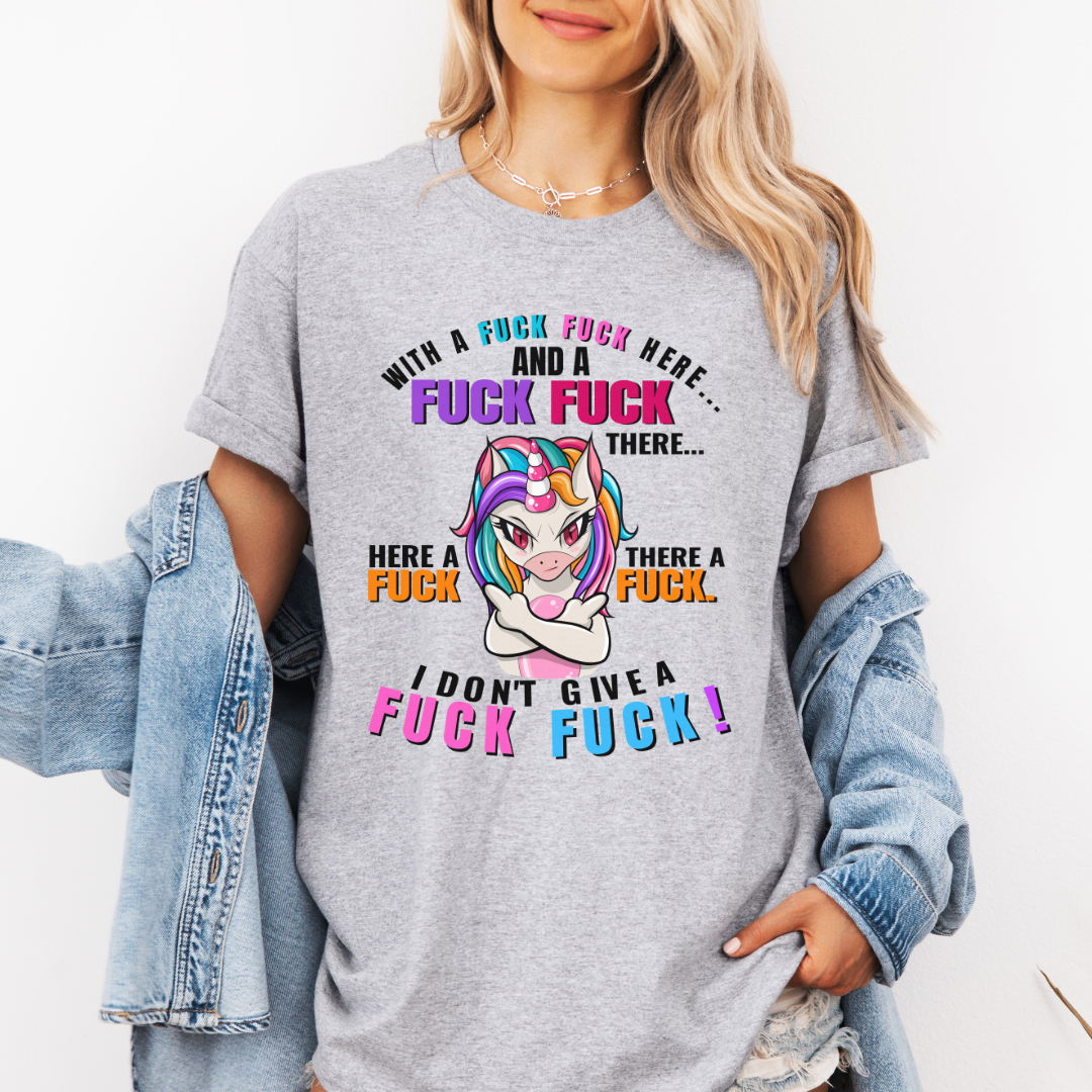 A woman wearing a grey graphic t-shirt with a colorful cartoon unicorn and bold profane text, "With a fuck fuck here… and a fuck fuck there… here a fuck, there a fuck… I don't give a fuck!", styled with an open light-wash denim jacket against a plain white background. From Coffee and Moo NZ