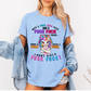A woman wearing a light blue graphic t-shirt with a colorful cartoon unicorn and bold profane text, "With a fuck fuck here… and a fuck fuck there… here a fuck, there a fuck… I don't give a fuck!", styled with an open light-wash denim jacket against a plain white background. From Coffee and Moo NZ