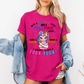 A woman wearing a bright pink graphic t-shirt with a colorful cartoon unicorn and bold profane text, "With a fuck fuck here… and a fuck fuck there… here a fuck, there a fuck… I don't give a fuck!", styled with an open light-wash denim jacket against a plain white background. From Coffee and Moo NZ